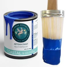 a blue paint can next to a brush with white bristles on it's side