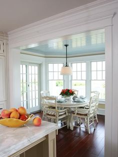 a bowl of fruit sitting on top of a kitchen counter next to a table with chairs