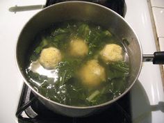 three balls of meatballs are cooking in a pot on the stove top, with broccoli and spinach