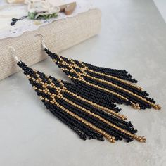 a pair of black and gold beaded earrings sitting on top of a white table