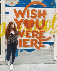 a woman standing in front of a wall with the words wish you were here painted on it