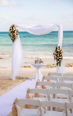 an outdoor wedding setup on the beach with white chairs and floral arrangements in front of the ocean