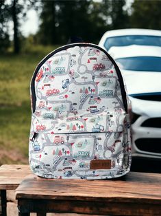 a backpack sitting on top of a wooden bench next to a white car and trees