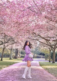 a woman in a purple dress and white boots standing under cherry blossom trees