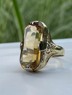 This is a lovely vintage Topaz cocktail ring, and what a darlin' she is. An 18k yellow gold band/setting with thick white gold prongs. The band features very organic, art nouveau-ish detailing. The Topaz is a smokey goldish color, which pairs beautifully with the colors in the band. Oh, that big ol' Topaz is 22 x 11mm. KAPOW! Please view the video for minor surface scratches to the topaz that are visible when viewing closely at certain angles. Not exceptionally noticeable. Details: Metal Purity Luxury Yellow Gold Topaz Ring In Art Deco Style, Luxury Vintage Topaz Ring Collectible, Luxury Unique Yellow Gold Topaz Ring, Vintage Luxury Topaz Ring Collectible, Luxury Yellow Gold Topaz Ring, Classic Yellow Gold Rings With High Luster, Formal Yellow Gold Rings With High Luster, High Luster Yellow Gold Rings For Formal Occasions, Classic High Luster Yellow Gold Rings