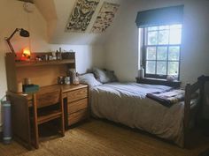 a bed sitting under a window next to a wooden desk