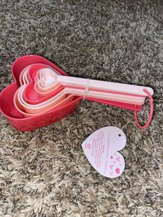 a heart shaped container with spoons in it on the floor next to some tags