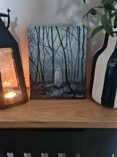 two lanterns are sitting on a table next to a painting with a ghost in the woods