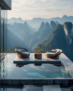 two lounge chairs sitting on top of a glass table next to a mountain side pool