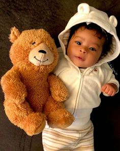 a baby is holding a teddy bear wearing a hoodie