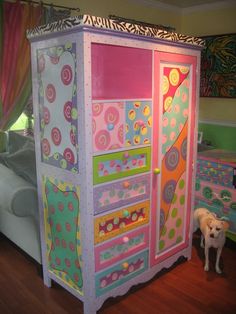 a dog standing in front of a brightly colored painted armoire with polka dots and circles on it