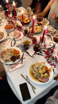 a long table is set with food and lit candles for christmas dinner guests to enjoy