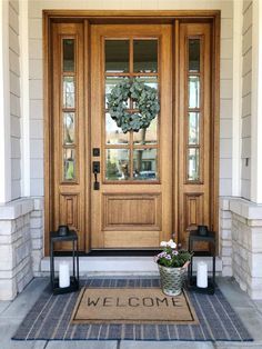 a front door with two lanterns and a welcome mat on the ground next to it