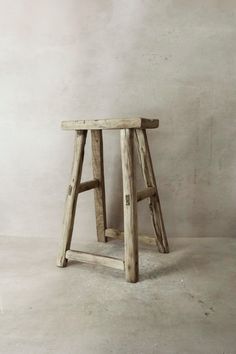 a small wooden stool sitting on top of a cement floor next to a white wall