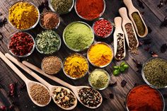 several spoons filled with different types of spices on top of a wooden table next to each other