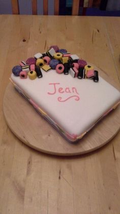 a birthday cake with the name jean spelled in small letters on it, sitting on top of a wooden table