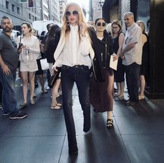 two women walking down the street in front of a group of people onlookers