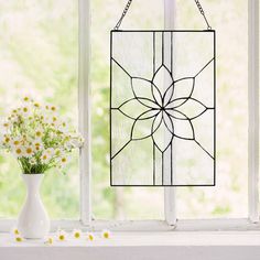 a vase with flowers sitting on a windowsill next to a window sill that has a stained glass sun catcher hanging from it