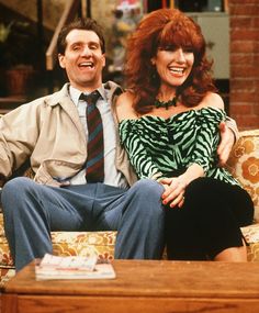 a man and woman sitting on a couch in front of a coffee table, smiling