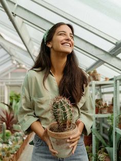 a smiling woman holding a potted cactus in a greenhouse