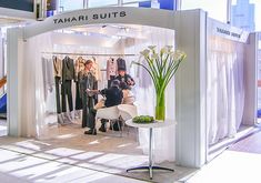 a man is standing in front of a booth at a fashion show with flowers on the table