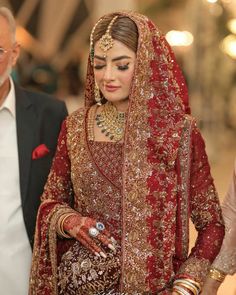 a woman in a red and gold bridal outfit walking down the aisle with an older man behind her