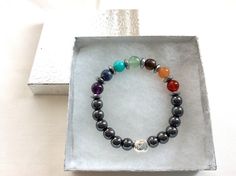 This Seven Chakra Energy bracelet includes authentic red jasper for the base chakra, carnelian for the sacral chakra, tiger eye for the solar plexus, green aventurine for the heart chakra, aquamarine for the throat chakra, lapis lazuli for the third eye and amethyst for the crown chakra. Activates and boosts your chakras to work in balance and greater power. Features a silver Buddha head charm and natural hematite 8mm beads for energy balance and protection. Anti-stress therapy. Available in thr Silver Hematite Jewelry For Healing, Healing Hematite Silver Jewelry, Silver Hypoallergenic Stretch Bracelet For Healing, Silver Hypoallergenic Stretch Bracelet, Spiritual Hematite Beaded Bracelet With Natural Stones, Hematite Round Beads Bracelets For Healing, Hematite Round Beads Bracelet For Healing, Hematite Beaded Bracelets With Natural Stones As Gift, Healing Hematite Bracelets With Natural Stones