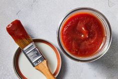 two tins filled with red sauce sitting on top of a white counter next to a wooden spatula