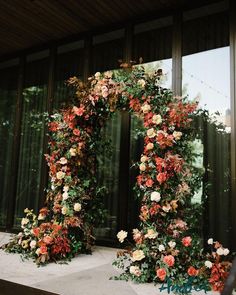 an arch made out of flowers and greenery in front of a large glass window