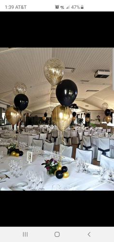 the table is set up with black and gold balloons, silver chairs, and white linens