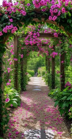 an archway covered in pink flowers and greenery next to a dirt path leading into a lush green forest