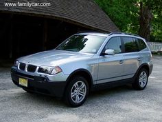 a silver car parked in front of a wooden structure with trees and bushes behind it