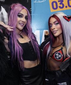 two beautiful women standing next to each other in front of a wall with signs on it