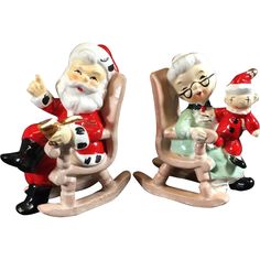 two figurines of santa and mrs claus sitting on rocking chairs, one holding a baby