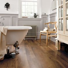 a bath tub sitting on top of a wooden floor next to a chair and mirror