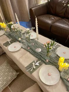 a long table with plates and candles on it in front of a brown leather couch