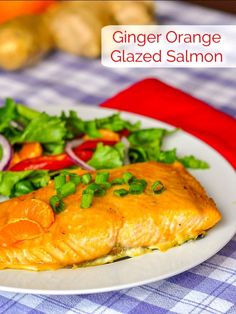 a white plate topped with salmon next to a salad