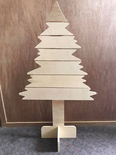 a wooden christmas tree on a stand in front of a wall