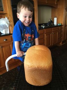 a young boy standing next to a large loaf of bread on top of a cooling rack