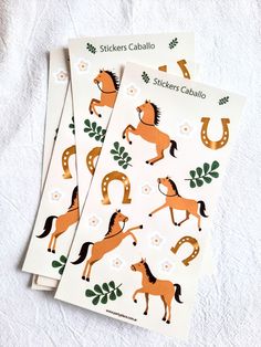 three stickers depicting horses and horseshoes on white paper with green leaves in the background