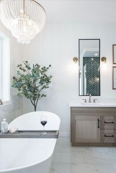 a white bath tub sitting next to a sink under a mirror and a chandelier