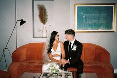 a bride and groom sitting on a couch in front of a coffee table with flowers