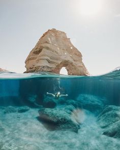 a person swimming in the ocean next to a rock formation