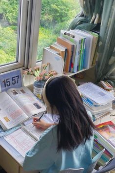 a woman sitting at a desk with books and papers in front of her, looking out the window