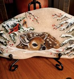 a deer sitting on top of a wooden table next to a bird and snow covered tree