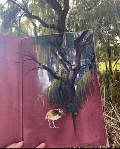 a person holding up a book with an image of a bird on it and trees in the background