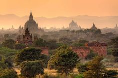 an ancient city surrounded by trees and mountains in the distance with foggy skies above