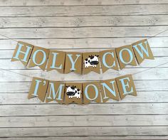 two brown and white cow themed banners on a wooden background with the words, holly cow i'm one