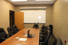 an empty conference room with black chairs and a projector screen in the corner on the wall