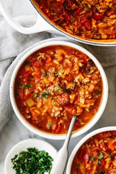 two white bowls filled with pasta and meat soup on a marble counter top next to a spoon